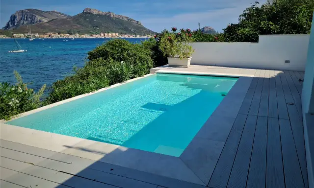 Piscina cristallina con vista mare. L'acqua, mantenuta con candeggina a un ph ideale, riflette il cielo azzurro e le montagne sullo sfondo.