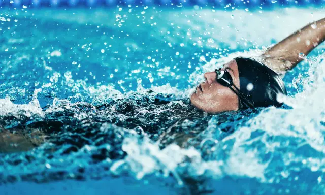 Atleta in nuoto dorso, godendo dei benefici di questo sport. L'acqua schizza intorno al suo viso concentrato.