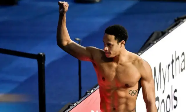 Shane Tusup, nuotatore con un pugno alzato, celebra una vittoria. Sul suo petto, i cinque cerchi olimpici.