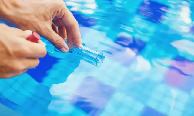 Mano che preleva campione d'acqua piscina con provetta. Il cloro basso indica necessità di trattamento.