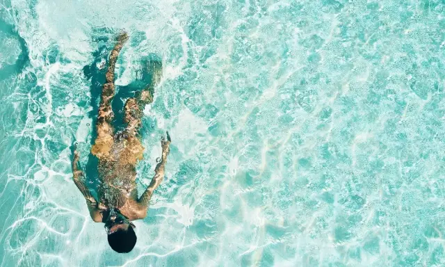 Persona sott'acqua in piscina, con riflessi luminosi. Chissà se il suo tatuaggio è fresco, dopo quanto tempo in piscina?