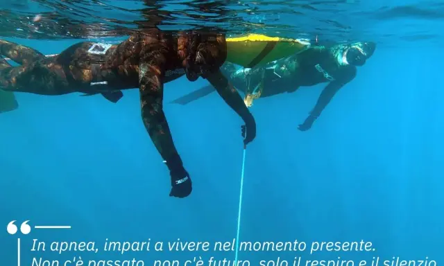 Due apneisti nuotano sott'acqua, uno vicino alla superficie. Imparare a trattenere il respiro, come rompere il fiato, porta a vivere il momento presente.