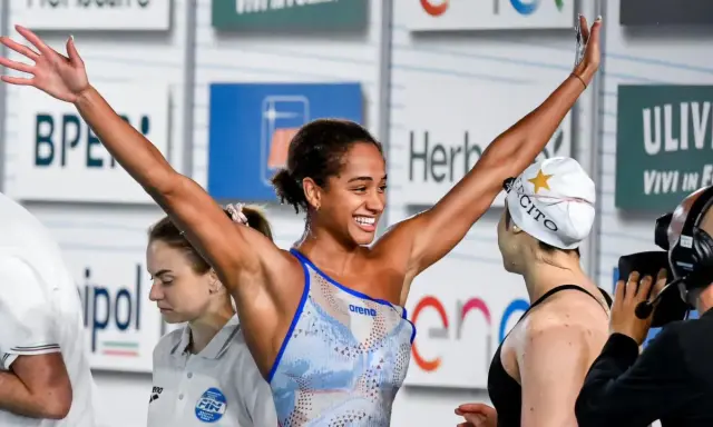 Atleta festeggia vittoria nel nuoto, braccia alzate con gioia.