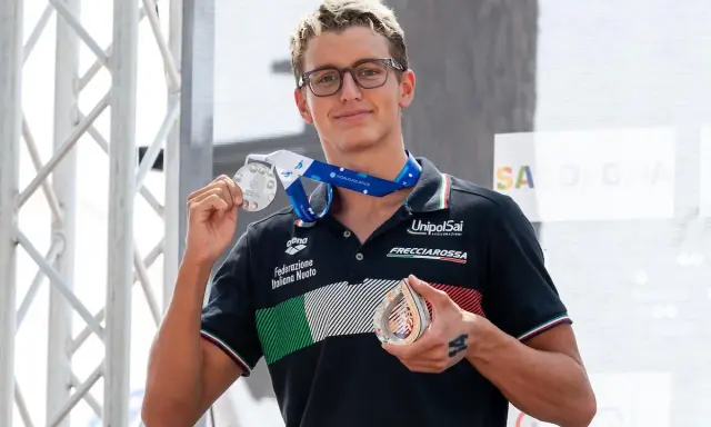 Davide Grossi, nuotatore italiano, mostra con orgoglio le sue medaglie d'argento e di bronzo, frutto di un'ottima prestazione.