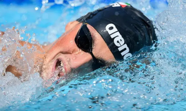 Nuotatore con cuffia Arena e occhialini, immerso nell'acqua con spruzzi. Potrebbe essere Pasquale Giordano in azione.