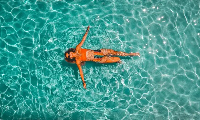 Donna rilassata galleggia in piscina. Il nuoto è un ottimo modo per migliorare la forma fisica, con risultati visibili nel nuoto cellulite prima e dopo.