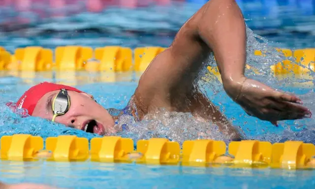 Nuotatrice con cuffia rossa e occhialini, in azione in piscina. Camille Muffat, un'atleta determinata.