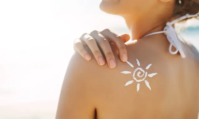 Sole sulla pelle, ma attenzione: il cloro toglie l'abbronzatura. Crema solare a forma di sole sulla spalla di una donna in spiaggia.