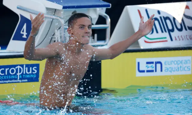 David Popovici esulta in piscina, circondato da schizzi d'acqua, con il numero 4 sulla corsia.