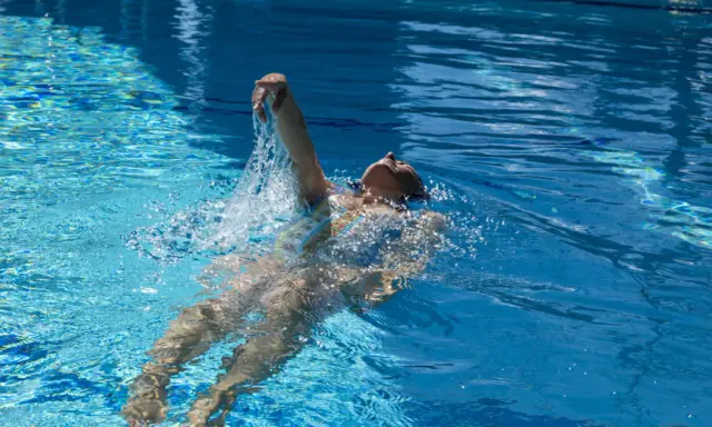 Donna nuota a dorso in una piscina olimpionica, godendosi la profondità e la frescura dell'acqua cristallina.