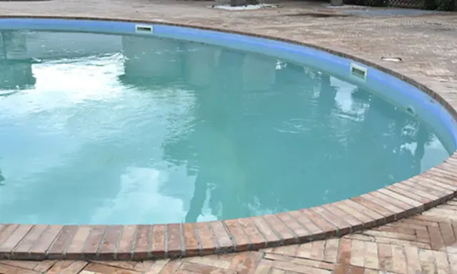 Piscina con acqua torbida e riflessi del cielo, circondata da un bordo in mattoni.