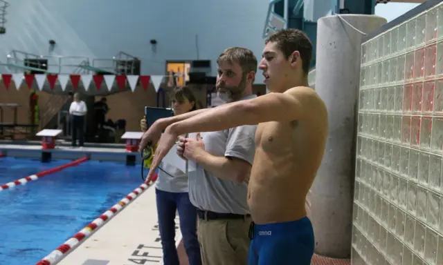Nuotatore pronto a gareggiare, forse Matt Grevers, con allenatori al bordo piscina.