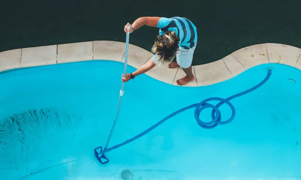 Ragazzo pulisce la piscina con un aspirafango piscina fai da te, rimuovendo detriti dal fondo azzurro.