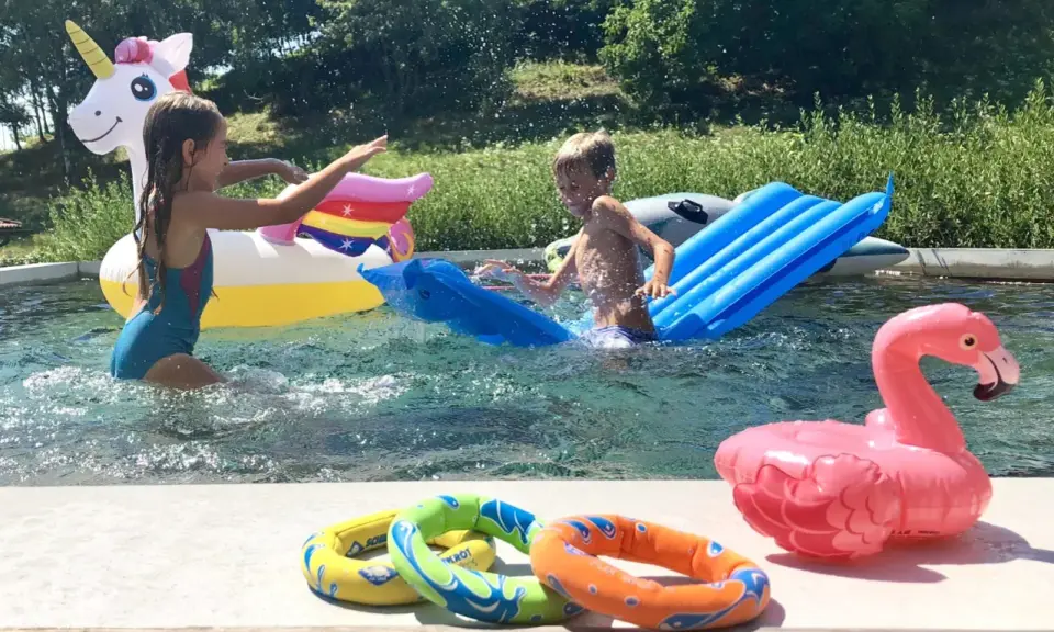 Bambini si divertono in piscina con gonfiabili colorati, tra cui un unicorno e un fenicottero. Perfetti giochi da fare in piscina senza niente per un'estate indimenticabile.