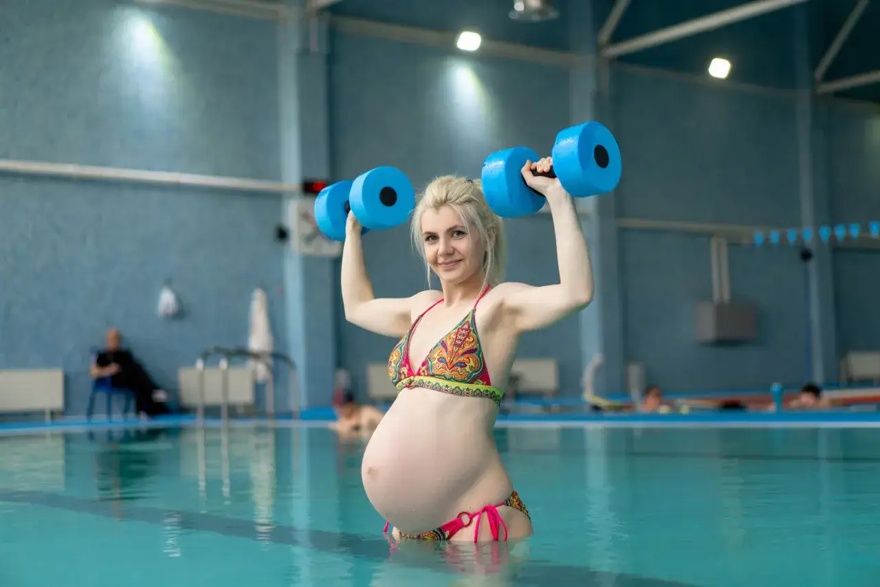 Donna incinta fa esercizi con pesi galleggianti in piscina. Il nuoto in gravidanza &egrave; un'ottima attivit&agrave; per mantenersi in forma.