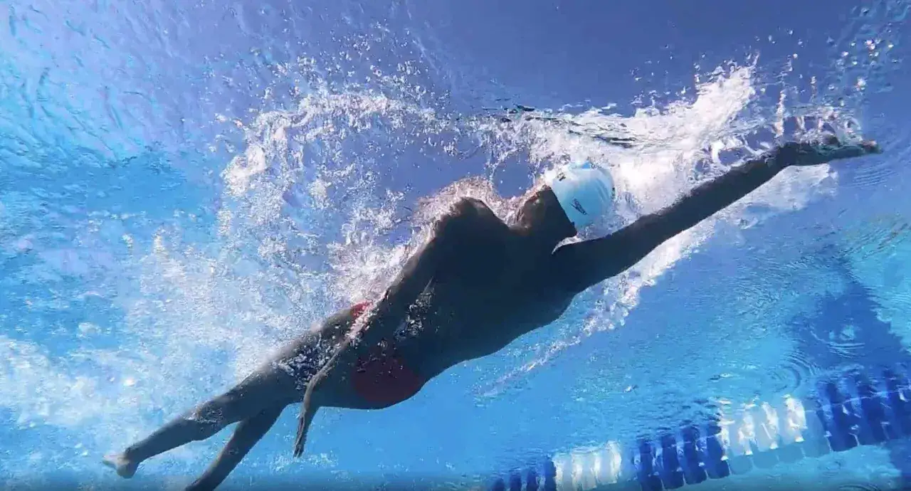 Nuotatore in azione, con la testa fuori dall'acqua e un braccio proteso in avanti, esegue una perfetta scheda dorso.