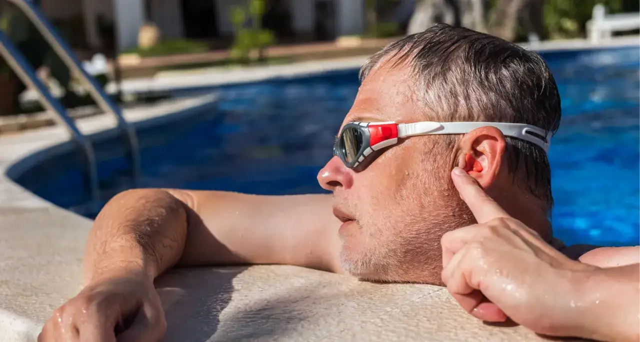Uomo con occhialini da nuoto inserisce tappi nell'orecchio, cercando rimedi per l'otite del nuotatore.