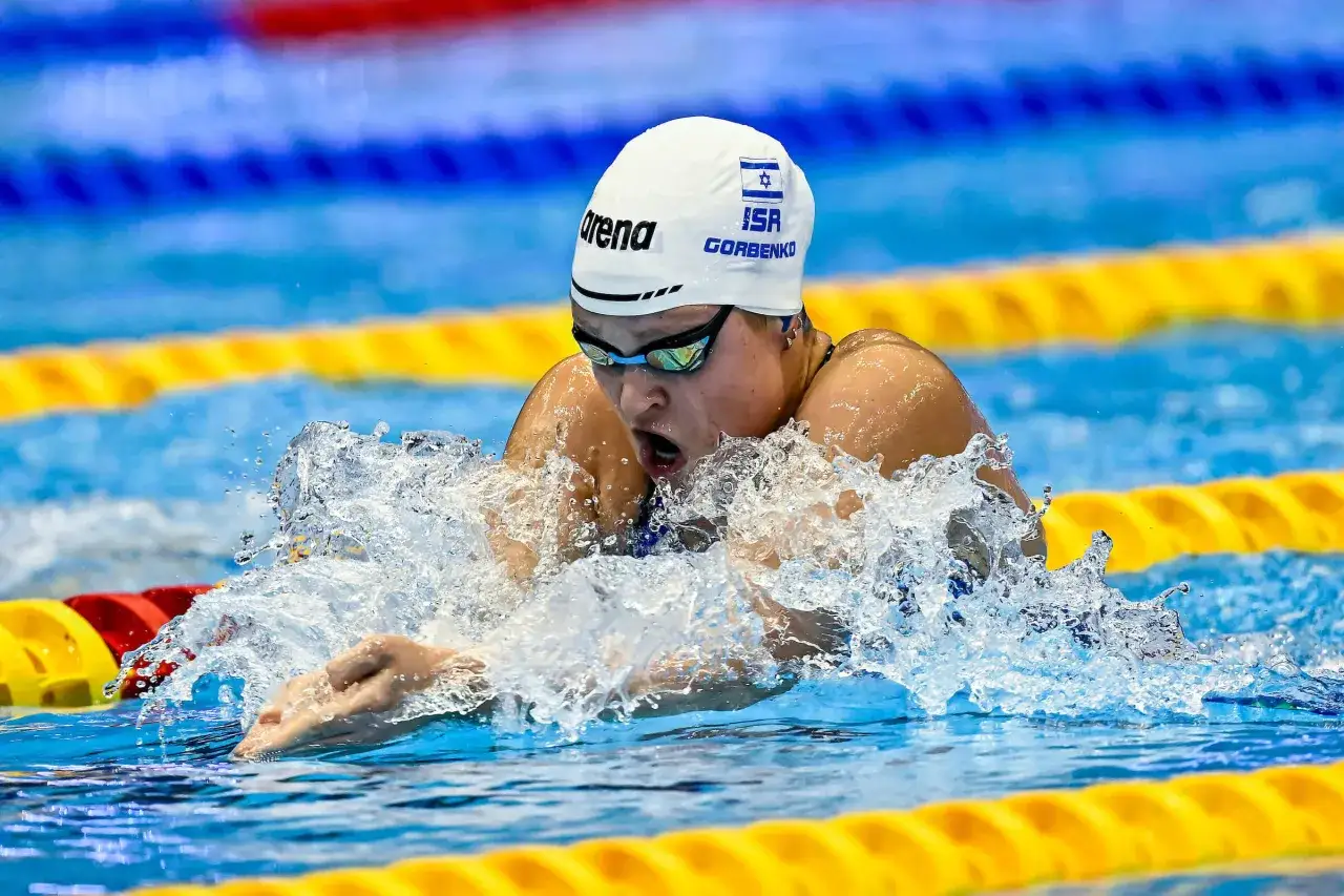 Anastasia Gorbenko in azione, con la cuffia ISR e gli occhialini, mentre nuota con vigore, sollevando spruzzi d'acqua.