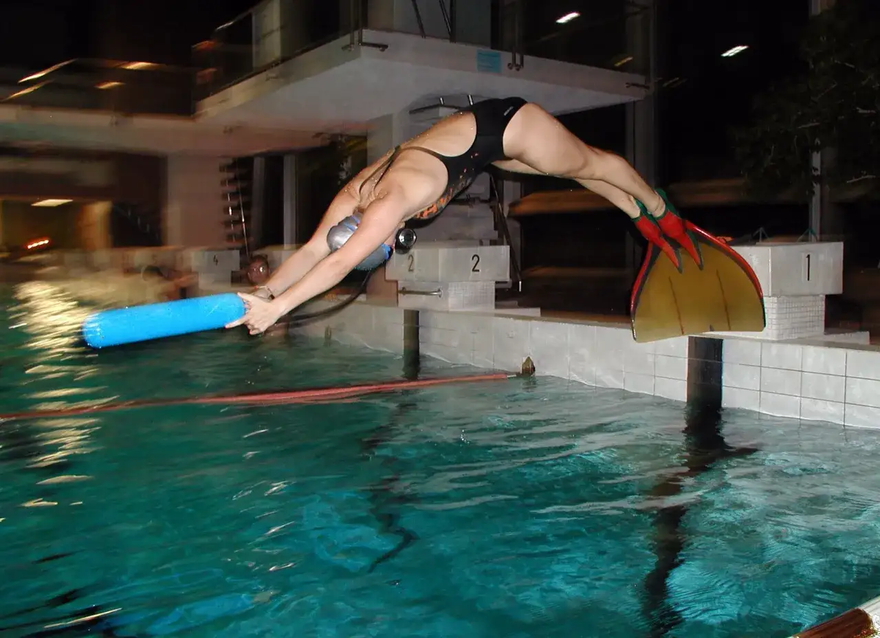 Nuotatrice con pinne corte rosse si tuffa in piscina, tenendo un galleggiante blu.