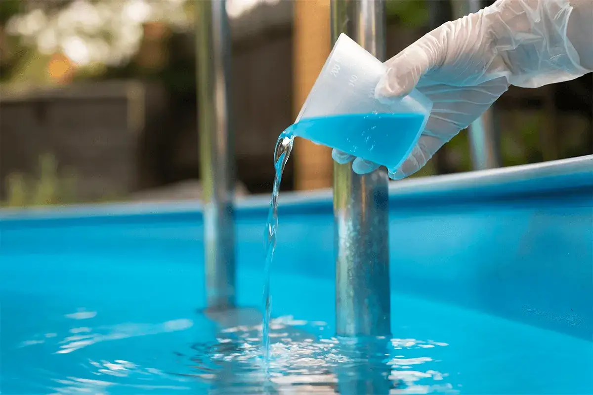 Mano con guanto versa liquido azzurro in piscina. Forse troppo antialghe in piscina, per evitare la formazione di alghe.