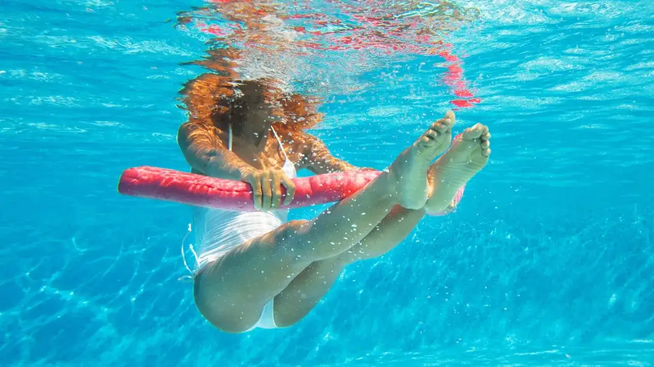 Donna esegue esercizi in acqua per dimagrire, usando un galleggiante rosso per allenare gambe e addome.