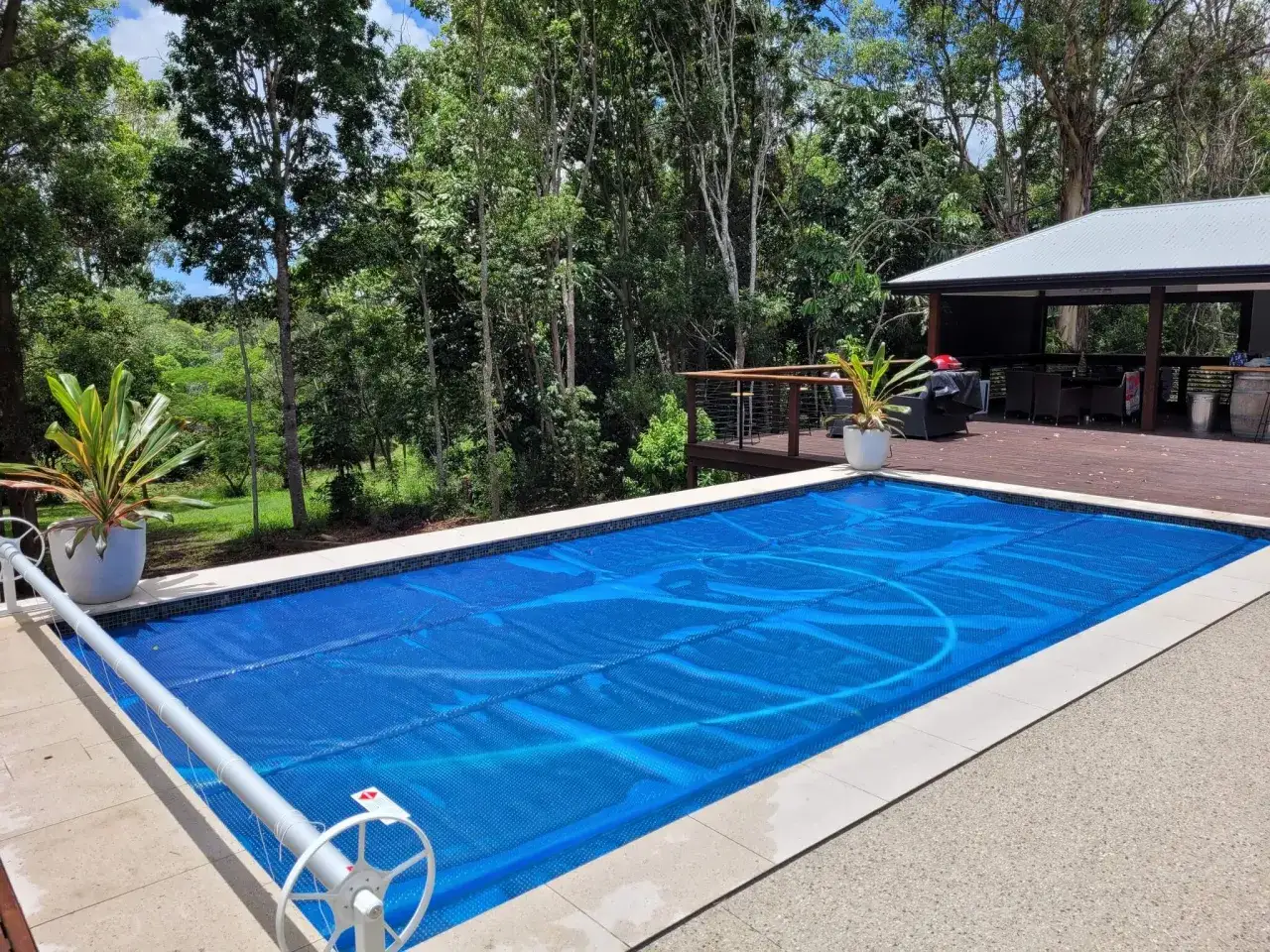 Copertura blu su piscina per ridurre l'evaporazione dell'acqua. La piscina &egrave; circondata da un bordo in pietra e da un prato verde.