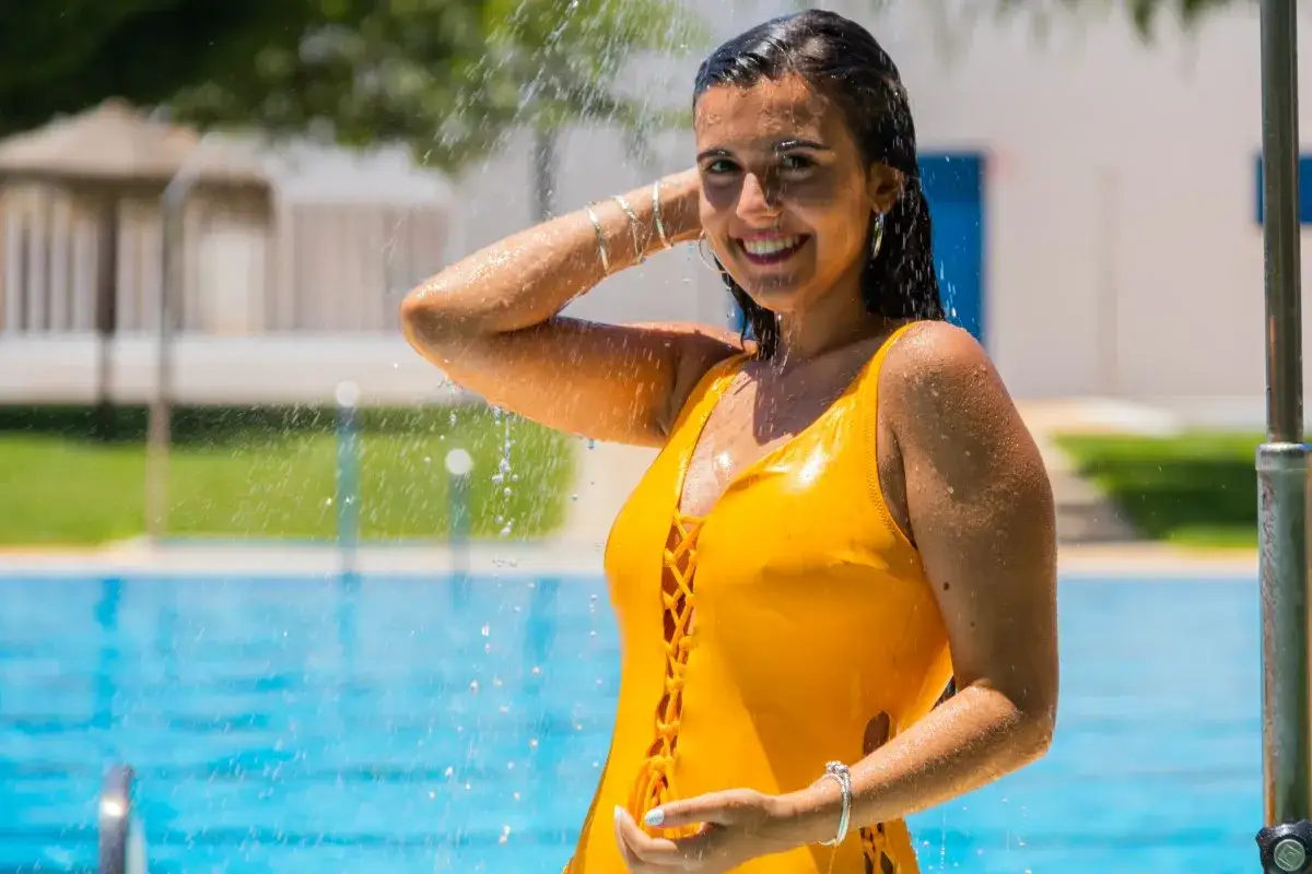 Ragazza sorridente sotto la doccia, con costume giallo, per alleviare il prurito dopo piscina.