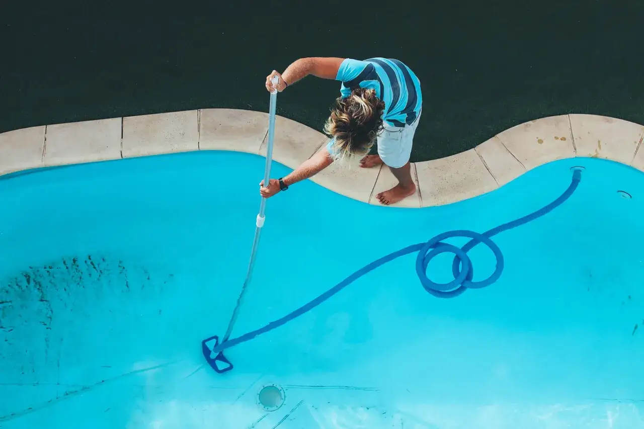 Ragazzo pulisce il fondo della piscina con un aspiratore, mostrando come pulire il fondo della piscina in modo efficace.