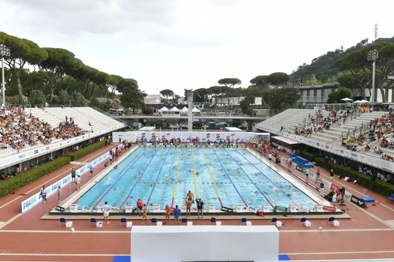Gara di nuoto con molti atleti in acqua e spettatori sugli spalti. Un evento di settecolli nuoto in una giornata luminosa.