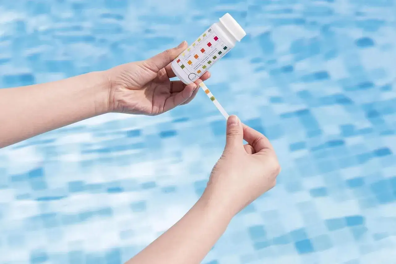 Mani che confrontano una striscia reattiva con la scala colorata per capire come controllare il pH della piscina.