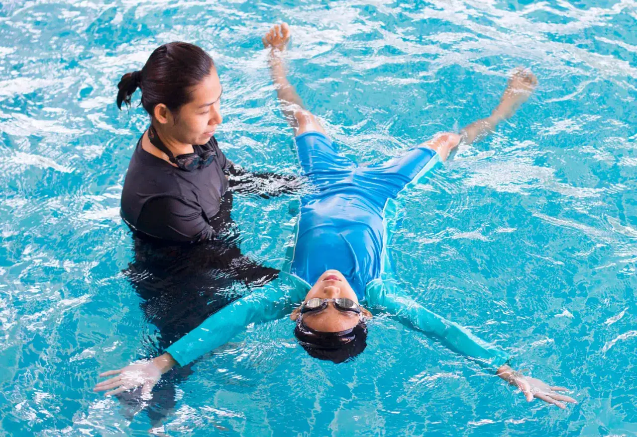 Un istruttore assiste un adulto che impara a nuotare a 40 anni, galleggiando sulla schiena in piscina.