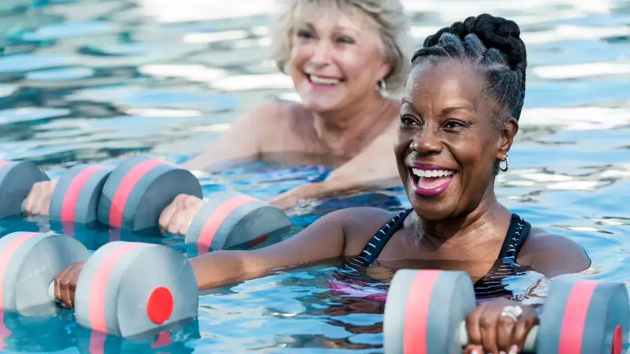 Donne sorridenti in piscina con pesi acquatici, godendosi i benefici del nuoto a 50 anni.