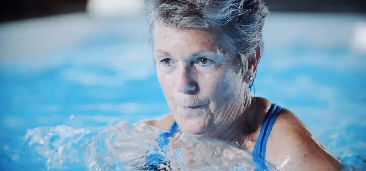 Donna anziana con capelli grigi si allena in piscina, un esempio di allenamento nuoto over 60.