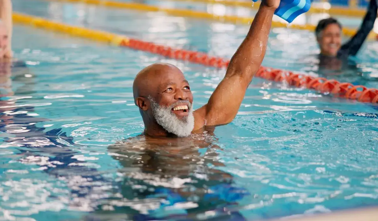 Uomo sorridente in piscina, con un braccio alzato, godendosi i benefici della piscina.