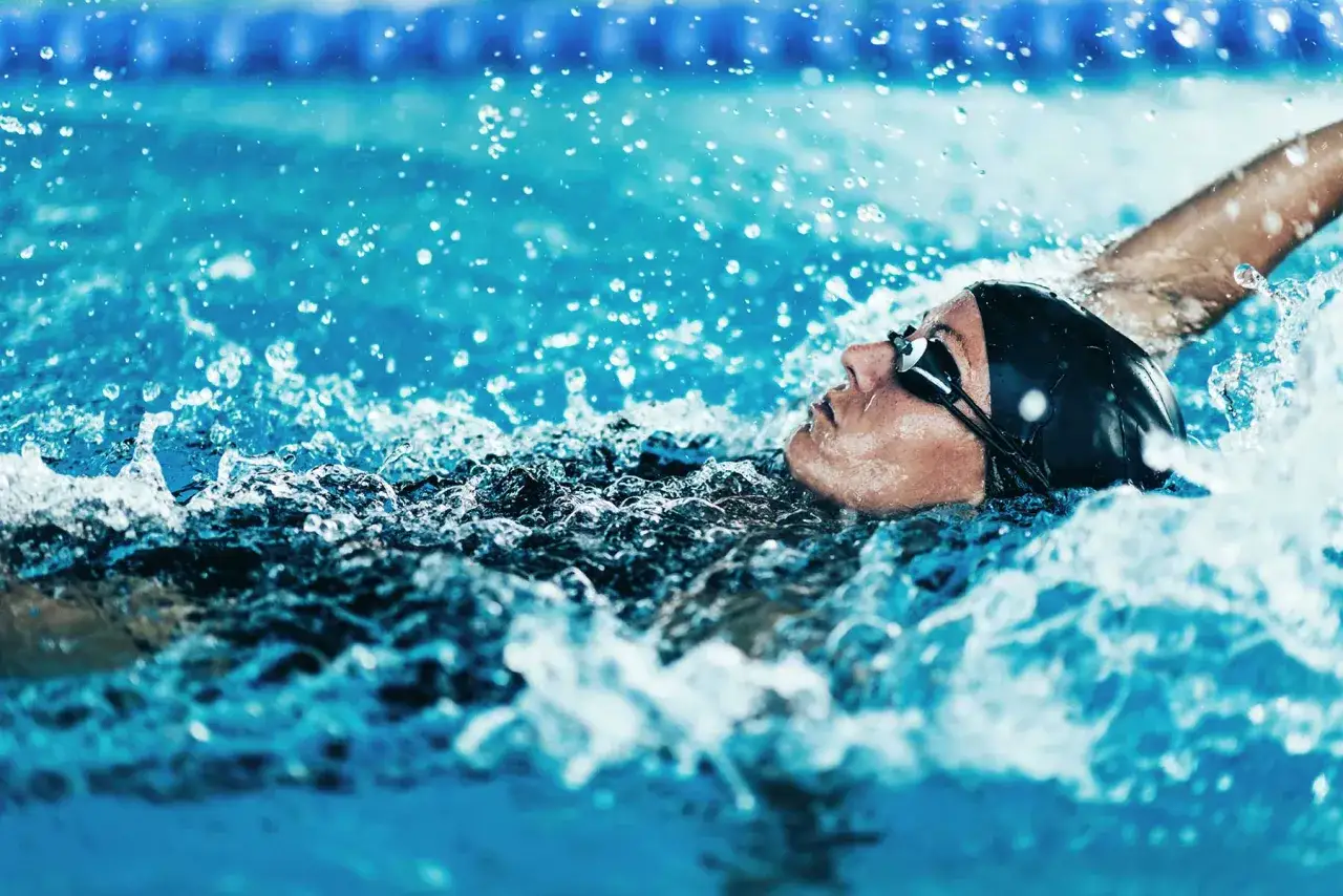 Atleta in nuoto dorso, godendo dei benefici di questo sport. L'acqua schizza intorno al suo viso concentrato.