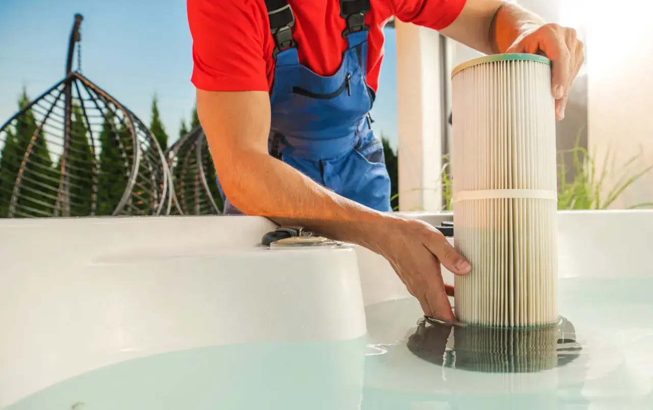 Un tecnico in tuta blu e maglia rossa rimuove un filtro dalla piscina, evitando la formazione di alghe.