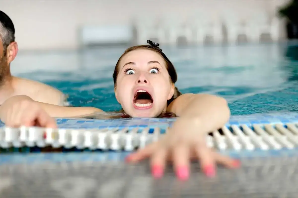 Donna spaventata in piscina, aggrappata al bordo. Una scena che illustra come vincere la paura dell'acqua da adulti.