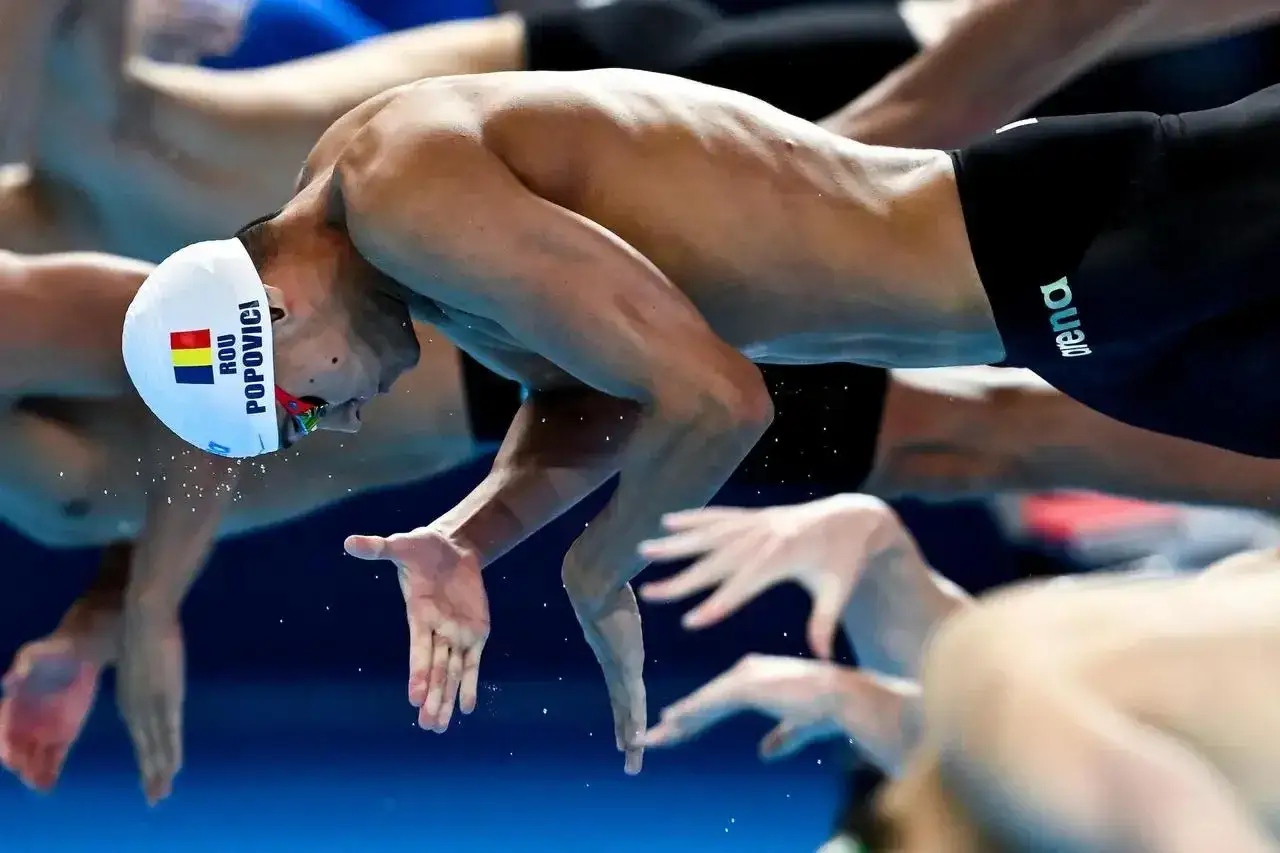 David Popovici in azione, con la cuffia che riporta la bandiera rumena e il suo nome, pronto a tuffarsi in piscina.