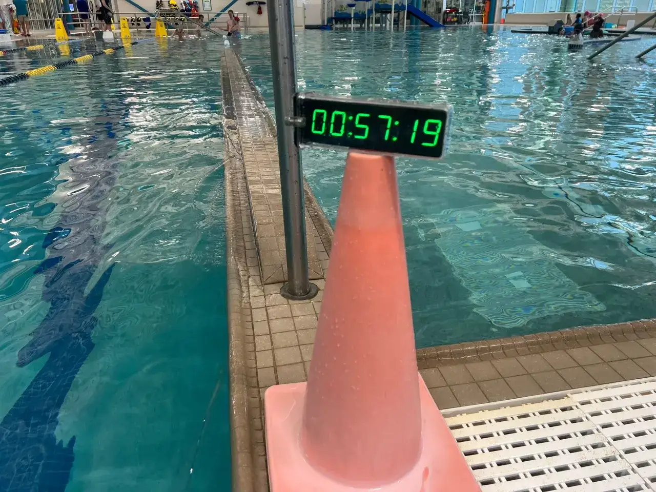 Cronometro in piscina mostra 00:57:19, utile per il calcolo passo nuoto. Cono rosa vicino al bordo.