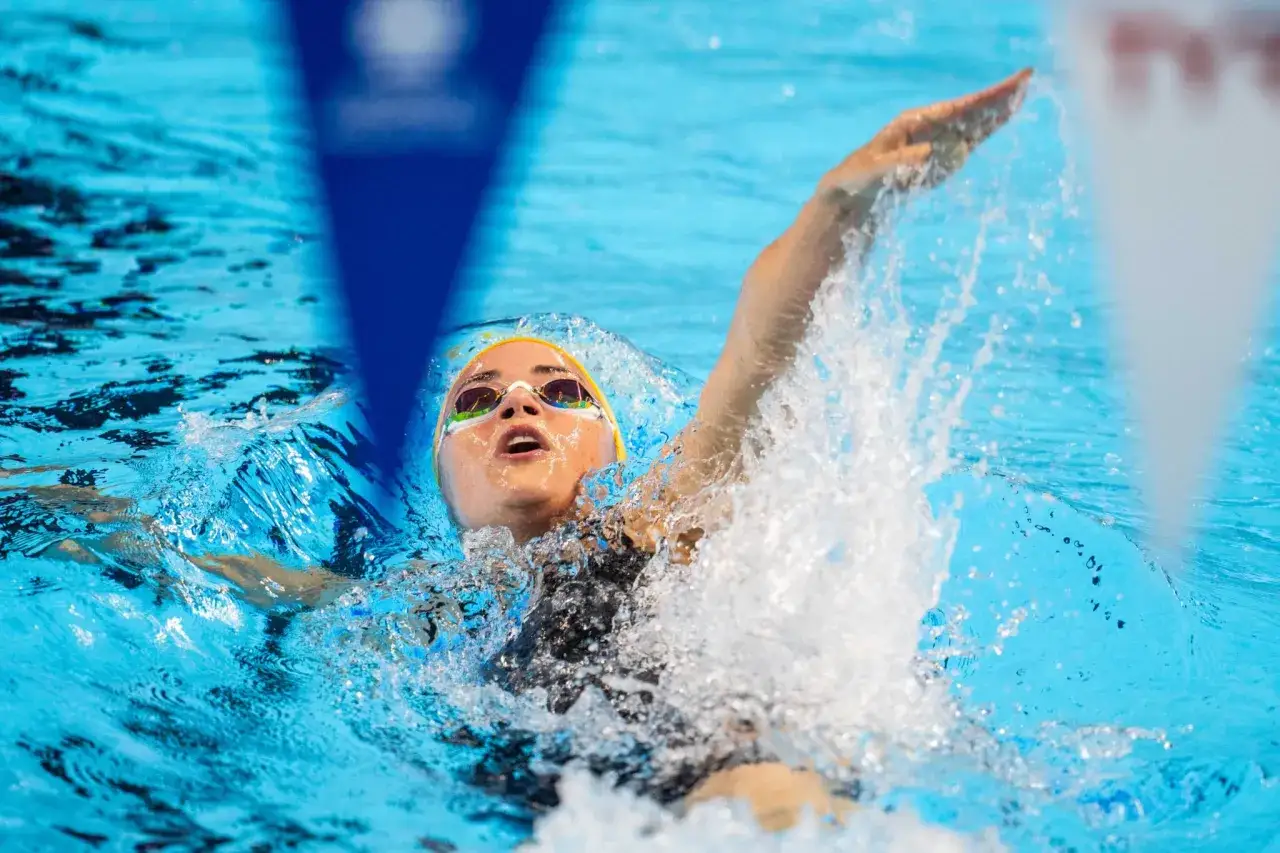 Kaylee McKeown nuota con determinazione, la testa fuori dall'acqua, gli occhi concentrati e la mano che fende l'acqua in una gara di nuoto.