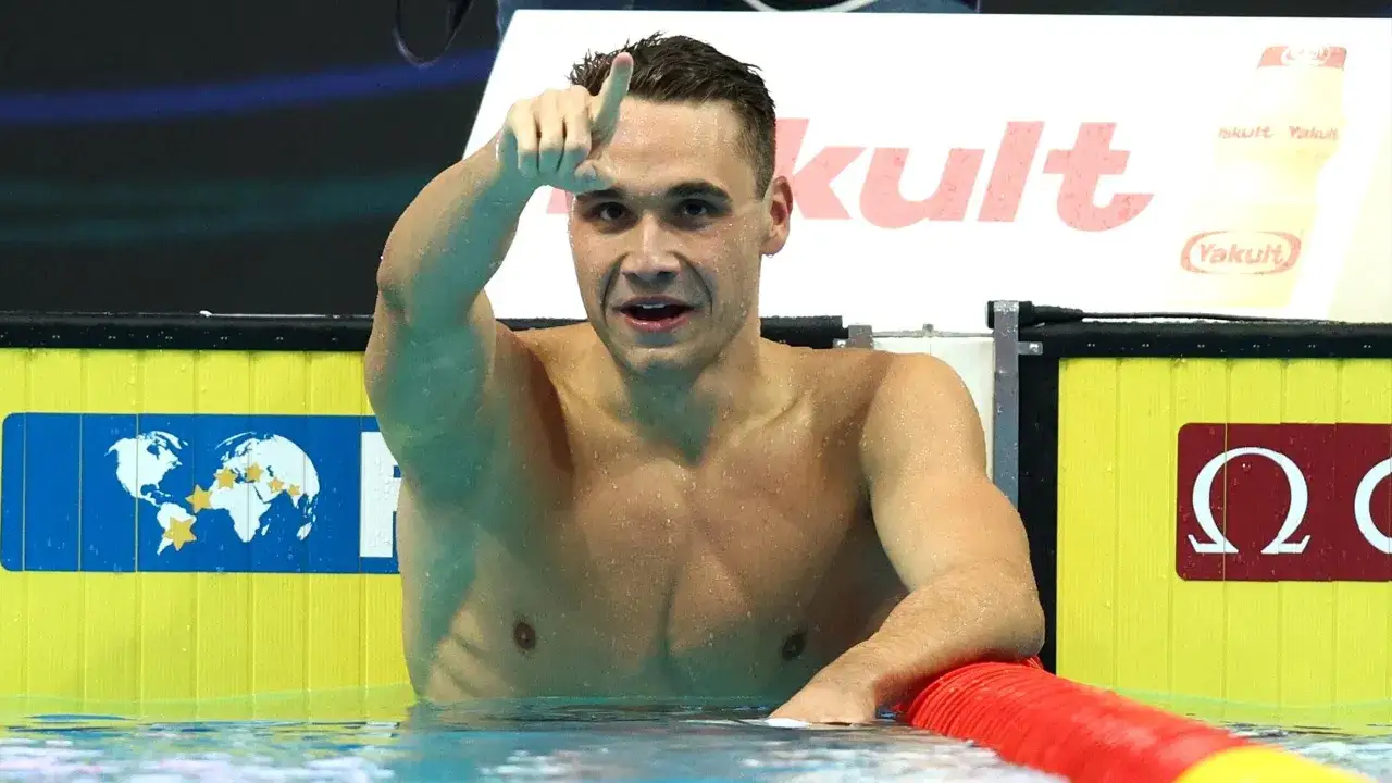 Kristof Milak, nuotatore ungherese, fa il segno di vittoria con il dito indice alzato, con alle spalle uno sfondo con il logo Yakult.