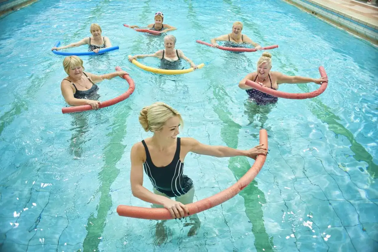 Donne sorridenti praticano ginnastica in acqua per mal di schiena, usando galleggianti colorati per esercizi di riabilitazione.
