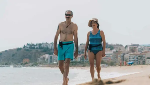 Coppia over 60 passeggia sulla spiaggia, un esempio di allenamento nuoto e vita attiva.