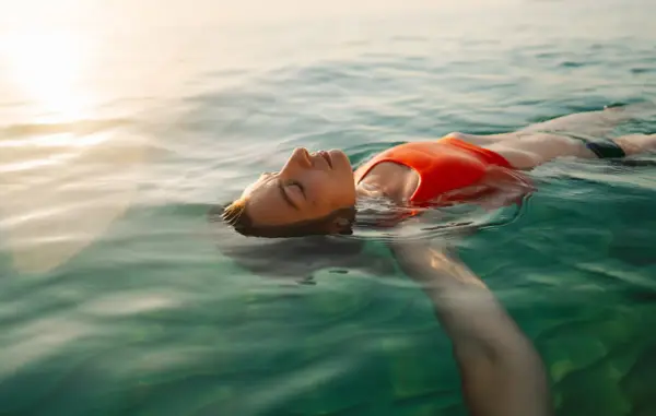 Donna galleggia serena in acqua cristallina, pensando ai rimedi per l'otite del nuotatore.