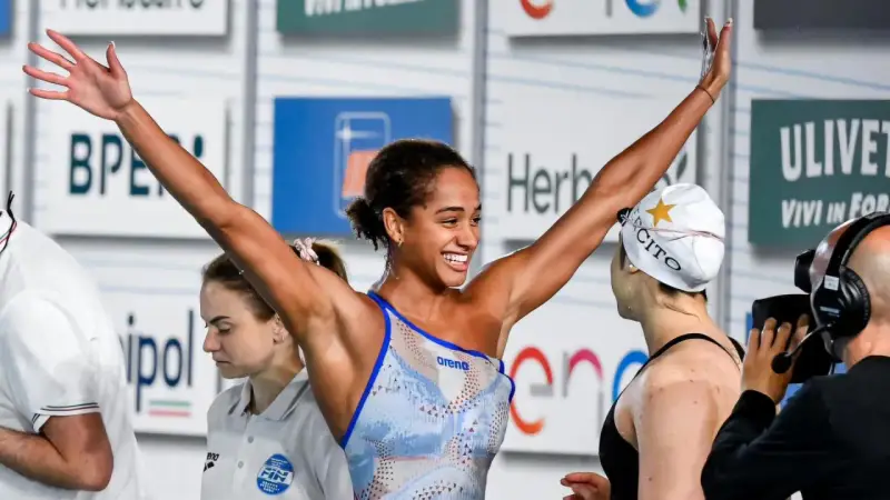 Atleta festeggia vittoria nel nuoto, braccia alzate con gioia.