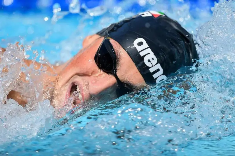 Nuotatore con cuffia Arena e occhialini, immerso nell'acqua con spruzzi. Potrebbe essere Pasquale Giordano in azione.
